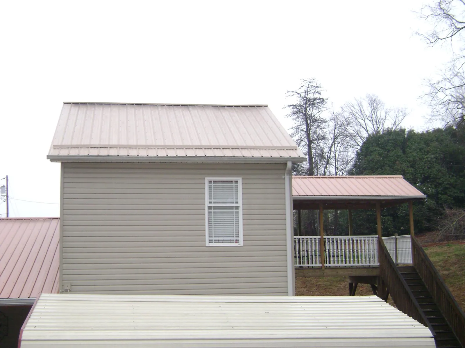 Tan metal roofs on a two story addition and attached porch, from a Roof Replacement job in Unionville